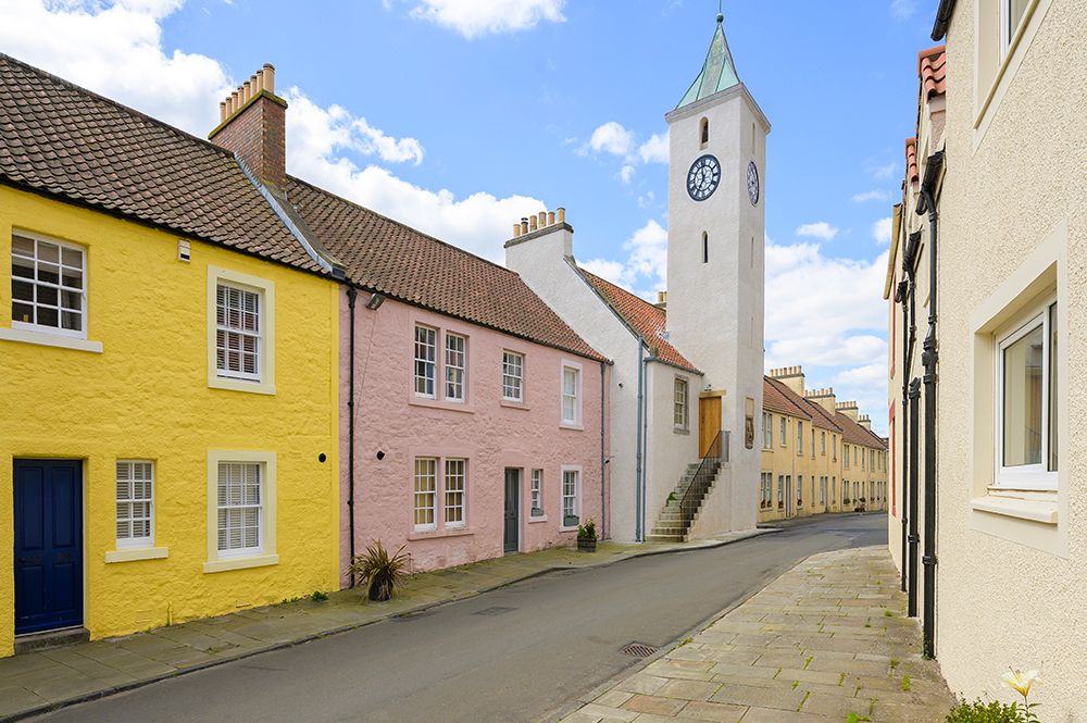 Colorful row of historic houses with yellow and pink facades along a quiet street with a white church spire in Scotland.