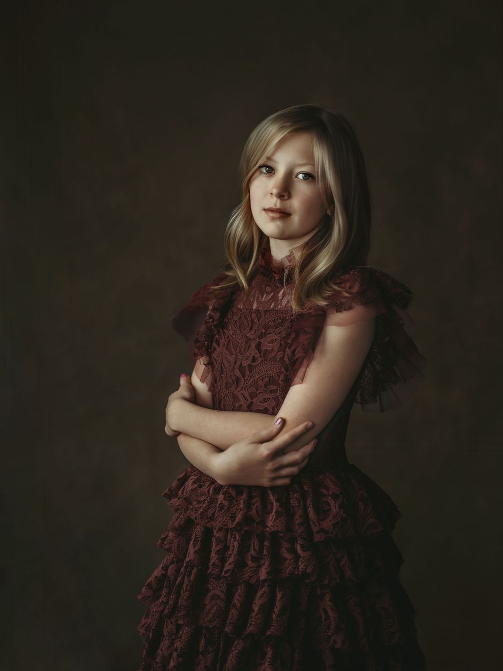 A moody portrait shows a child in a burgundy lace dress against a dark background.