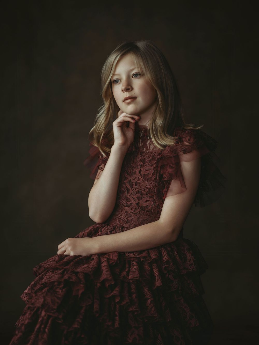 A series of moody portrait photographs showing a child in a burgundy dress against a dark background.