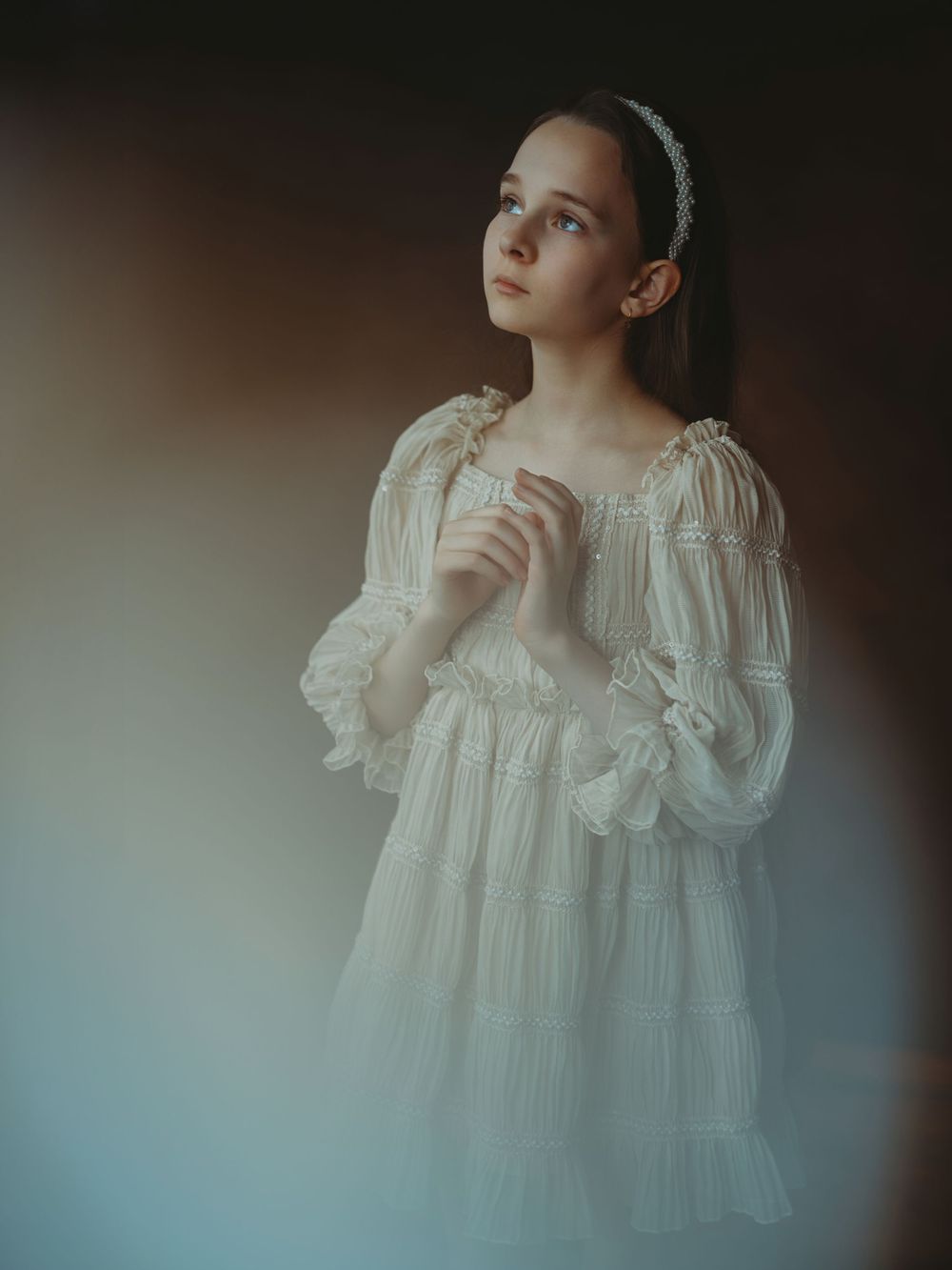 A person in a vintage-style white lace dress poses against a dark background in a dreamy portrait series.