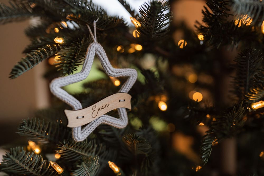 A silver star-shaped ornament hangs on a Christmas tree with twinkling lights in the background.