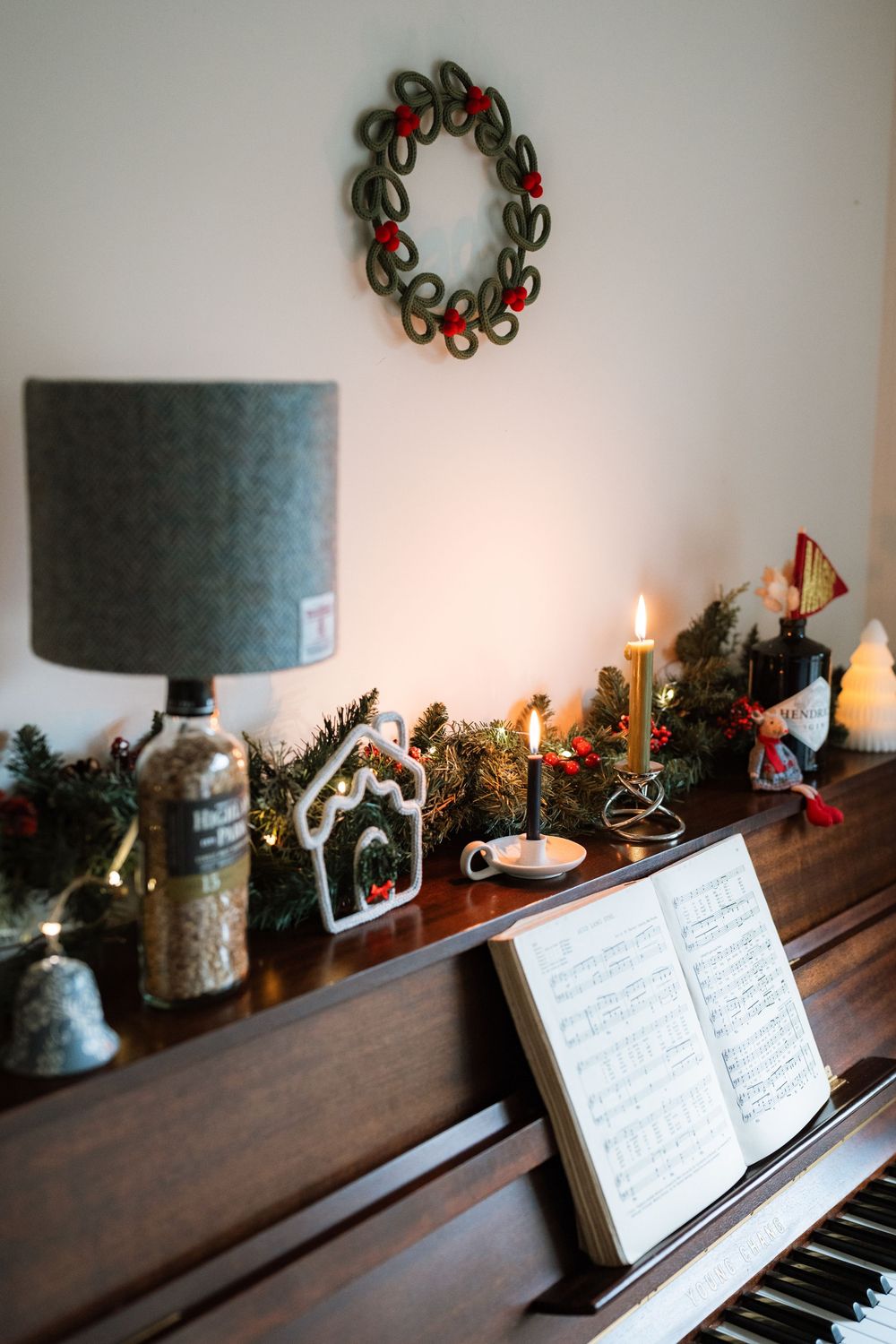 A piano decorated for Christmas with candles, sheet music, and evergreen decorations along its wooden top.