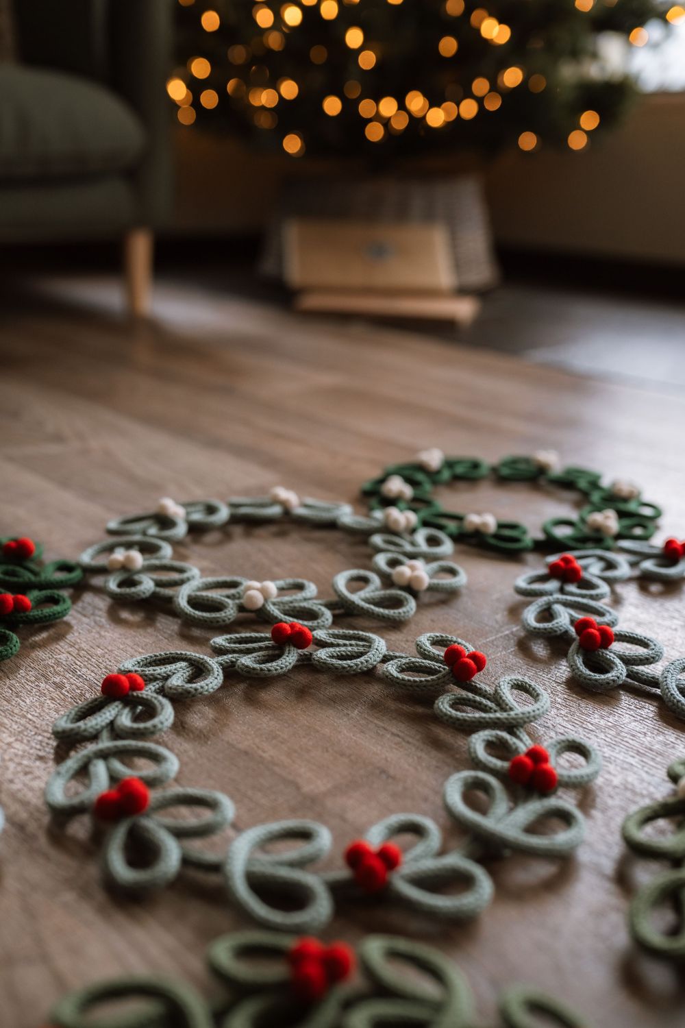 Close-up of a handmade Christmas wreath decoration with green loops and red berries on a wooden surface.