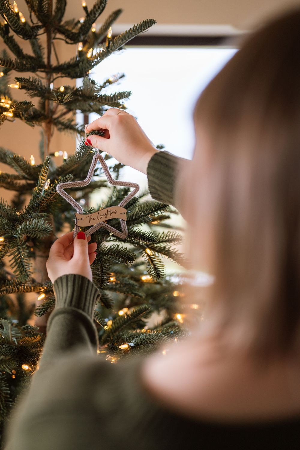 Close-up view of hands decorating a Christmas tree with twinkling lights in the background.