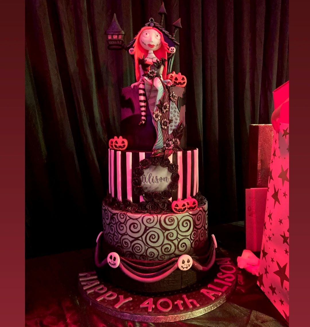 A black and pink gothic-themed birthday cake with spiral decorations and ornate details illuminated by red lighting.