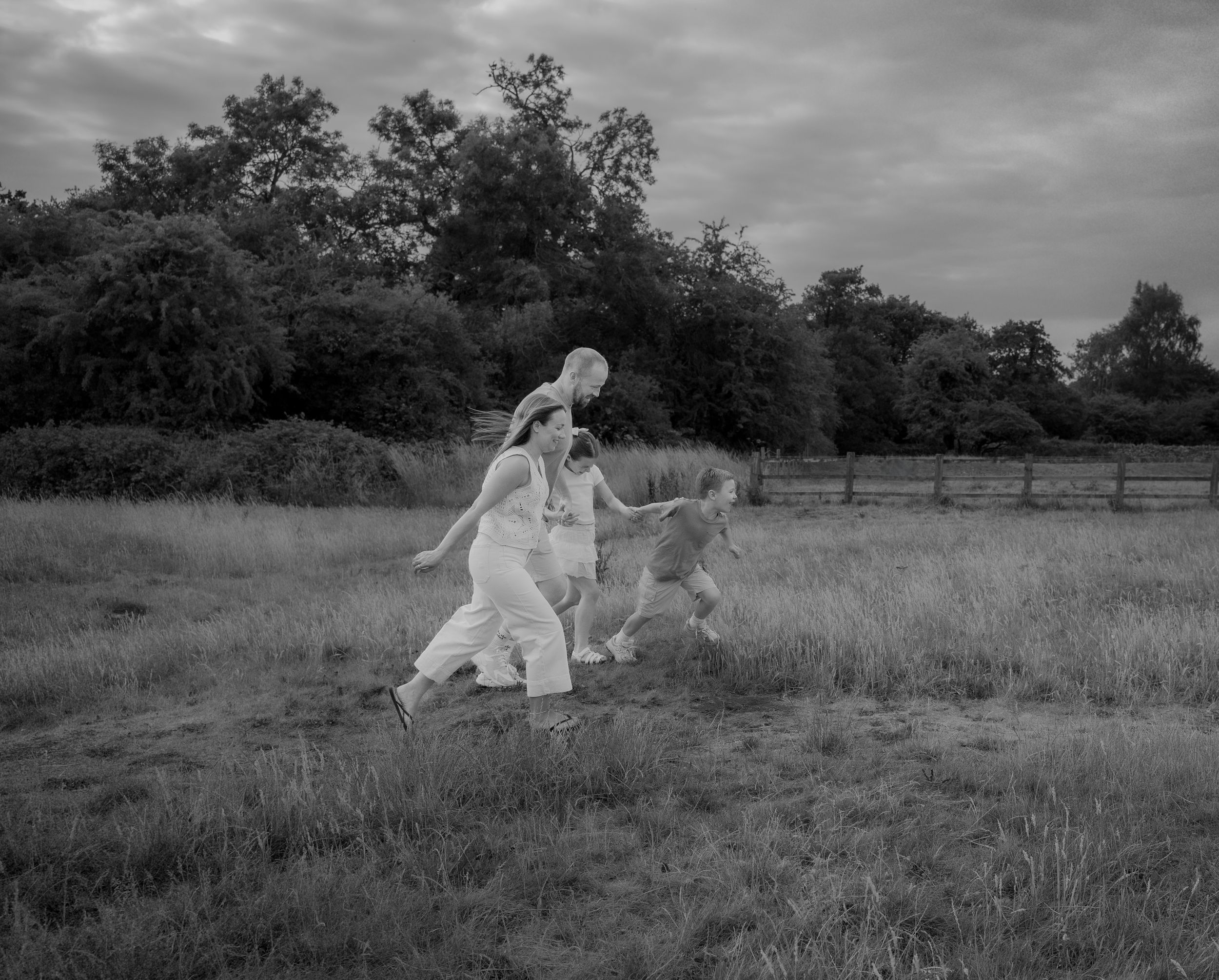A black and white photograph shows people in flowing white clothing running through a grassy meadow at dusk.