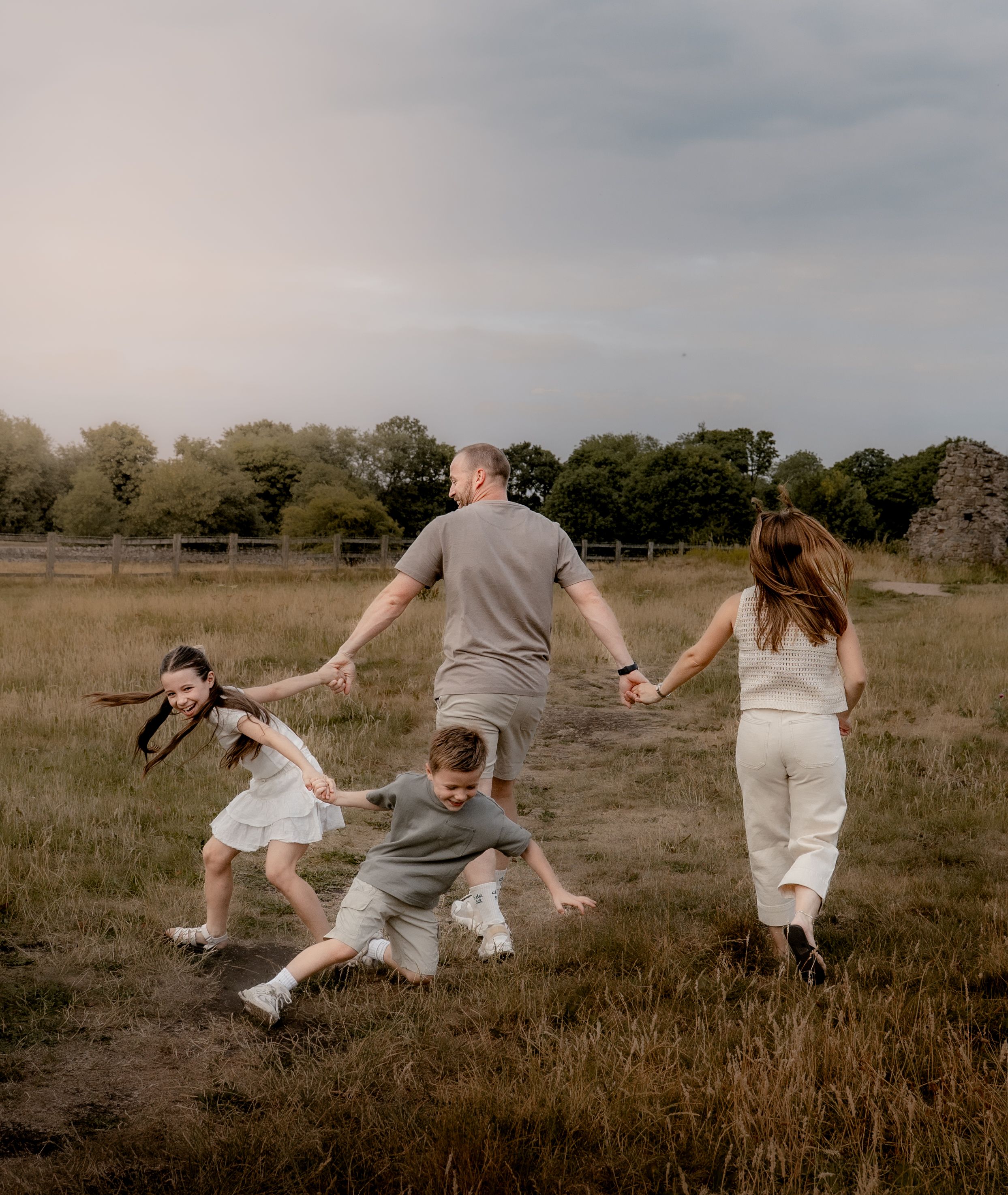 People holding hands and running together through a grassy field at sunset with trees in the background.