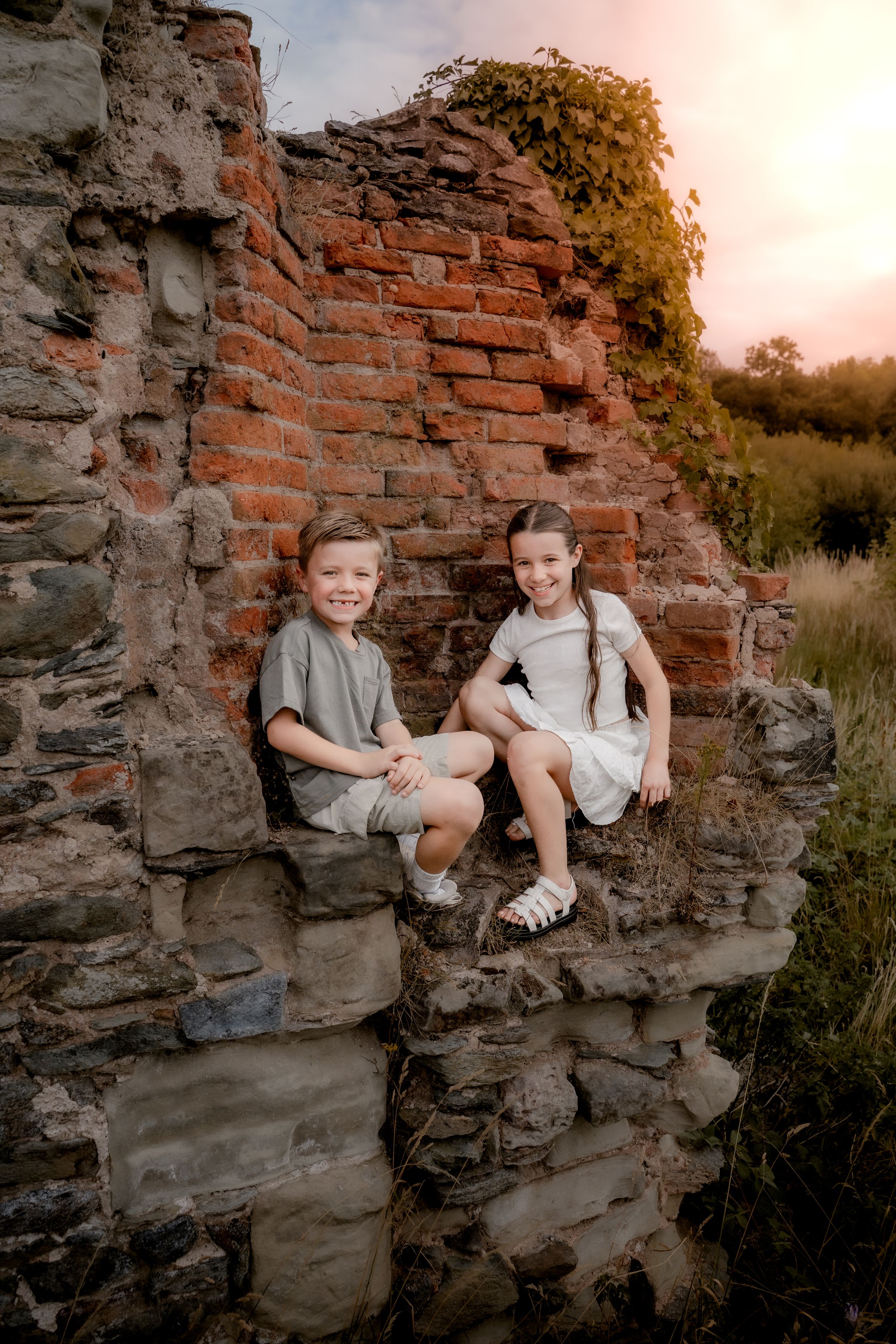 Two children sit together on old brick ruins at sunset in a rustic outdoor setting.