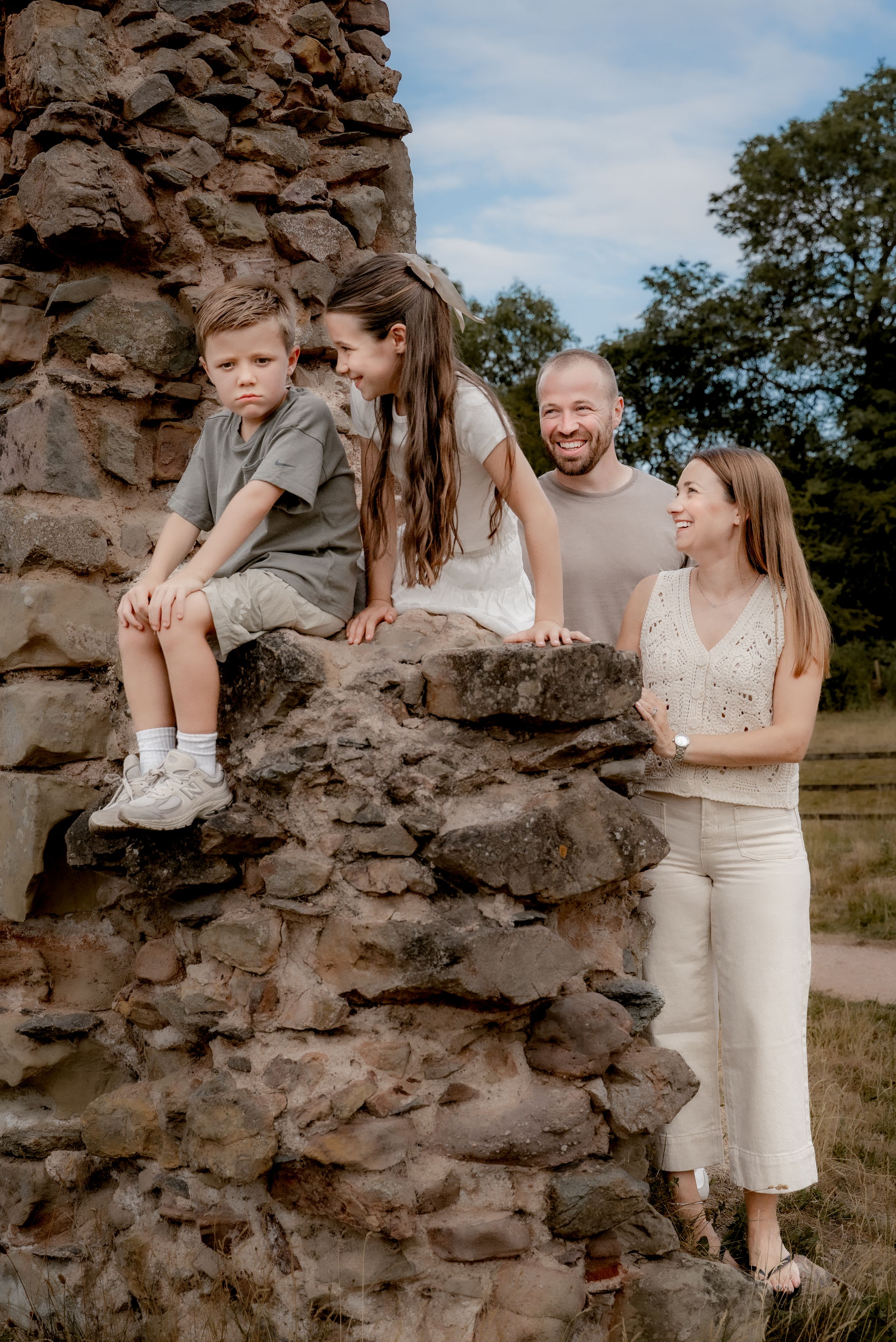 A family shares playful moments together while posing among stone ruins on a sunny summer day.
