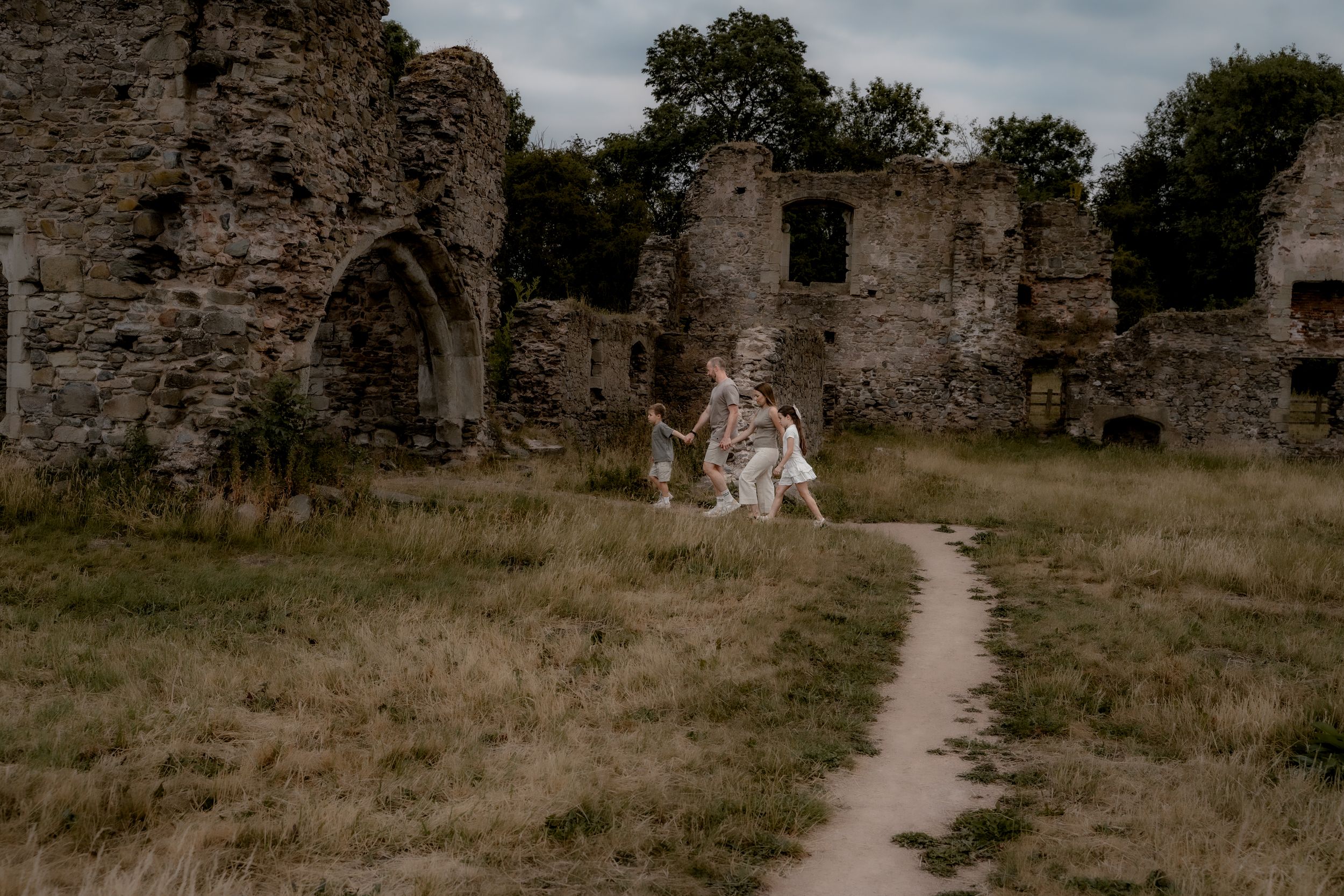 A stone path leads through the ruins of an ancient castle with crumbling stone walls and grassy grounds.