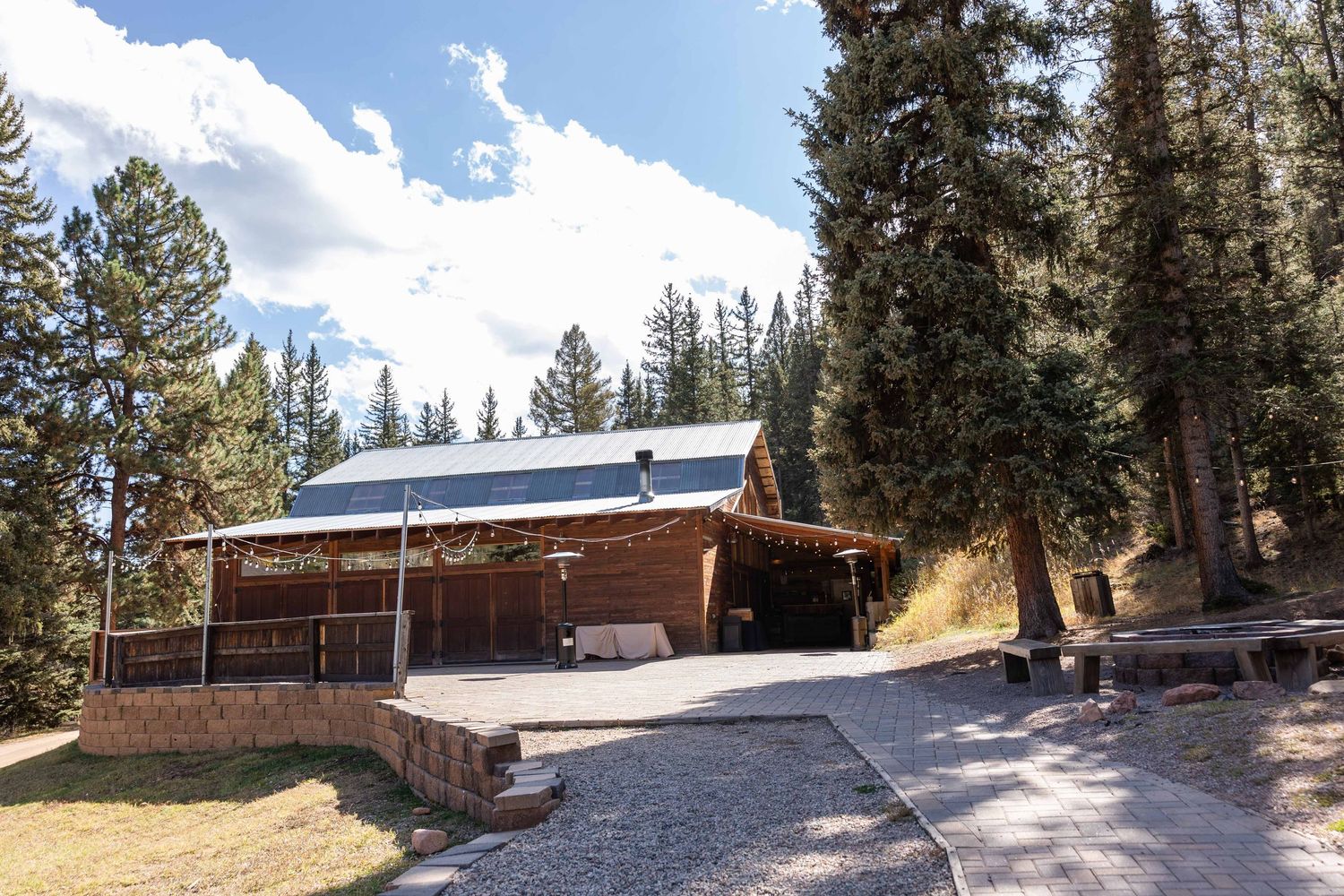 A scenic mountain cabin with wooden exterior sits nestled among tall pine trees in a snowy forest landscape.
