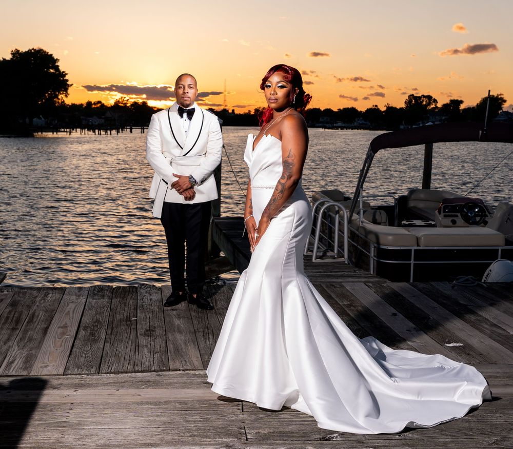 A romantic sunset wedding photoshoot on a wooden dock with a couple in white formal attire by the water.