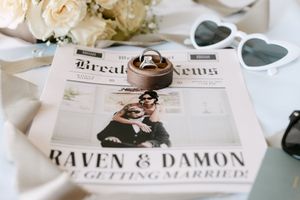 Elegant wedding stationery and decor details featuring ivory roses, rings, and printed invitations laid out on white surface.