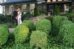 A couple shares a romantic moment in a lush garden setting with green hedges and bushes surrounding them.