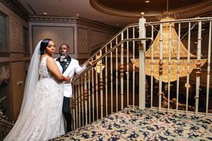 A wedding couple shares a romantic dance moment near an elegant staircase with a chandelier in the background.