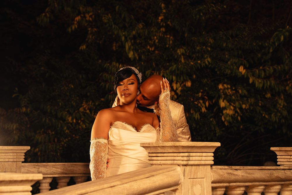 A romantic wedding couple embraces and kisses on a stone balustrade at sunset during their outdoor photoshoot.