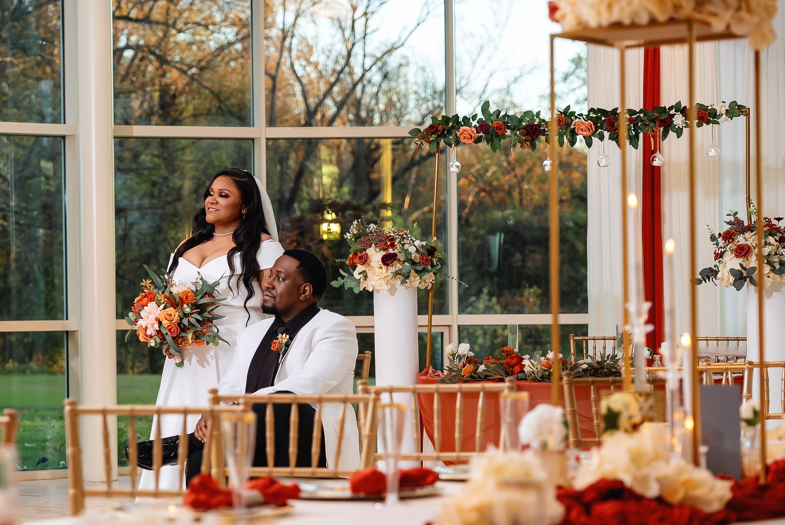 A panoramic view of a wedding reception venue with elegant floral arrangements and white decor in a sunlit glass room.