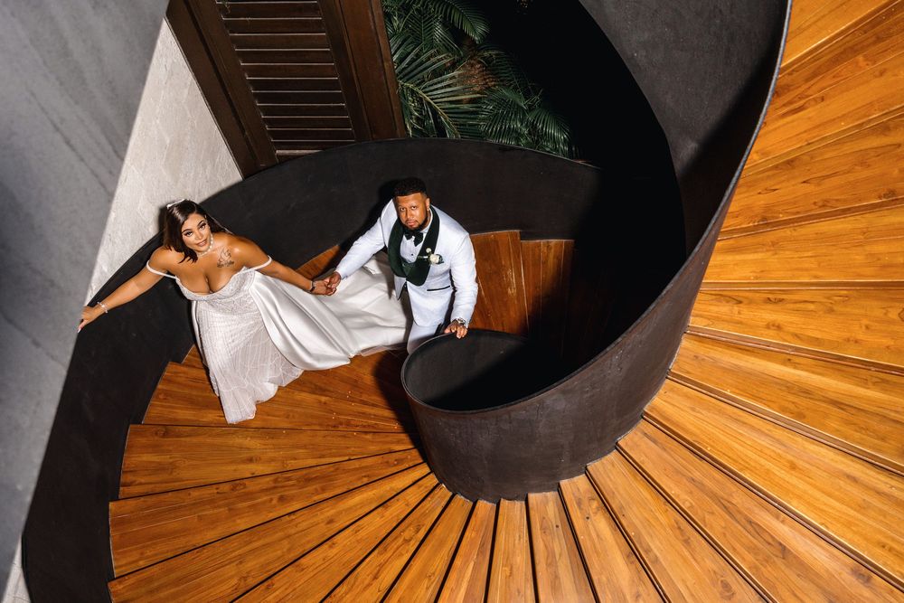 A bride and groom pose on a dramatic spiral staircase with wooden steps and dark curved walls.