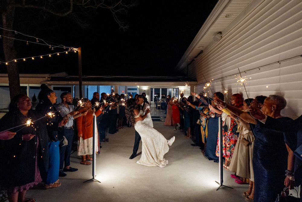 Wedding guests hold sparklers creating a magical tunnel of light for a couple during their nighttime send-off celebration.