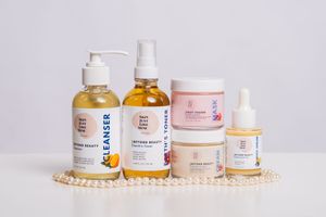 Beauty and skincare products arranged in a row on a white surface with a delicate pearl necklace.