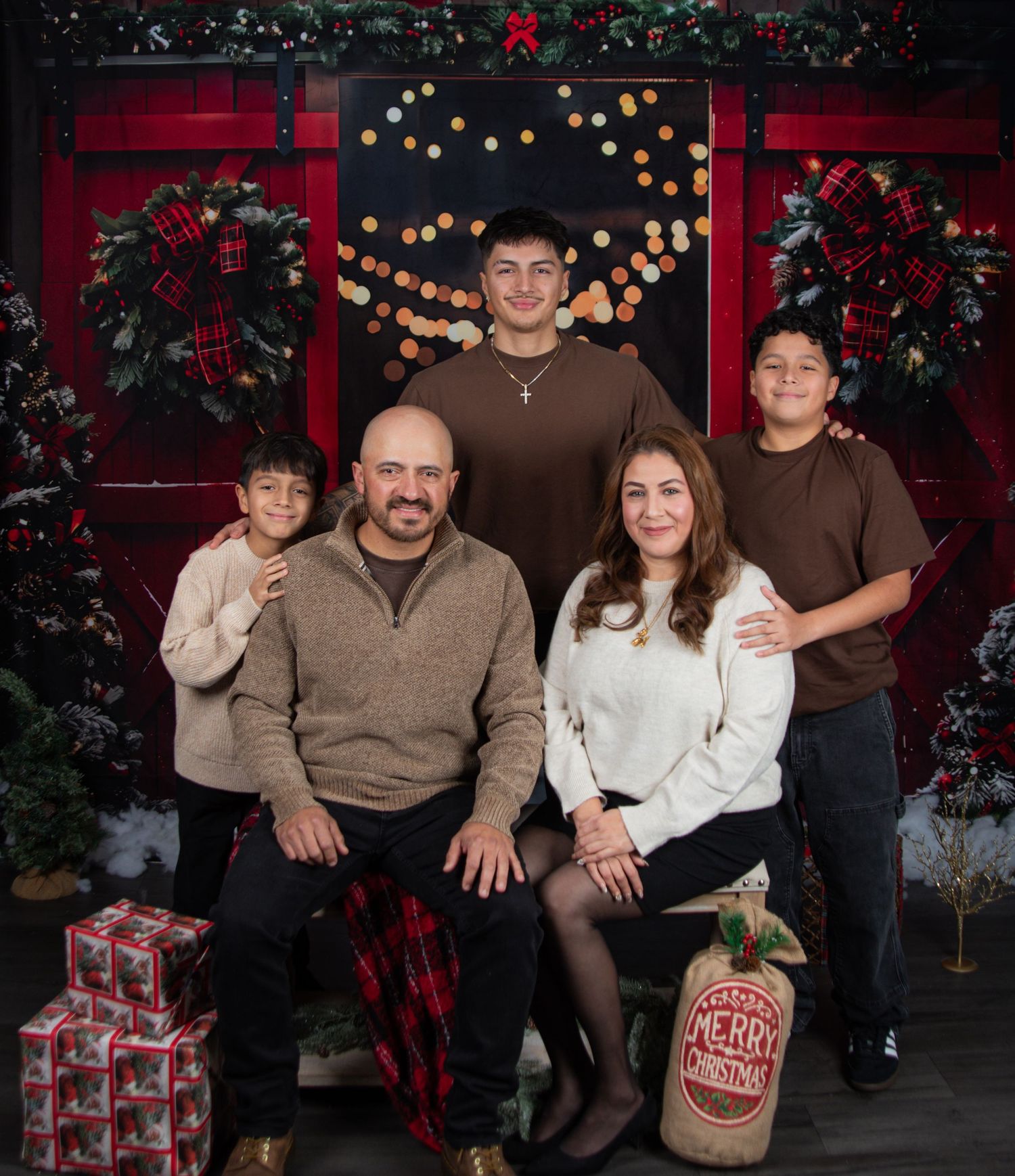 Family poses together for holiday photos in front of festive red backdrop with twinkling lights and Christmas decorations.