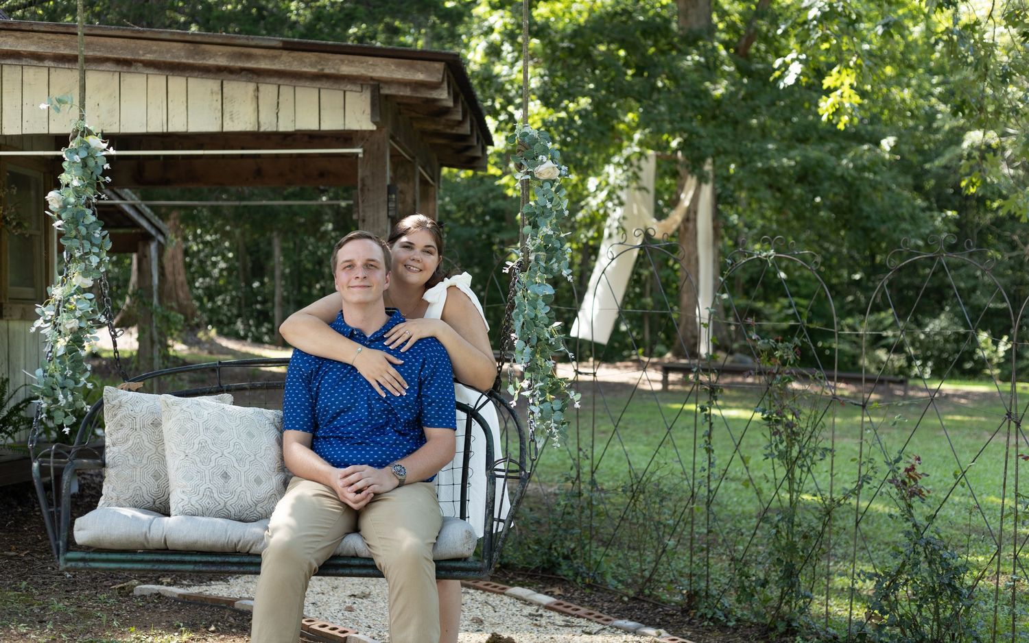 A couple sits together on a rustic wooden porch swing in a peaceful garden setting at a wedding venue in North Alabama.