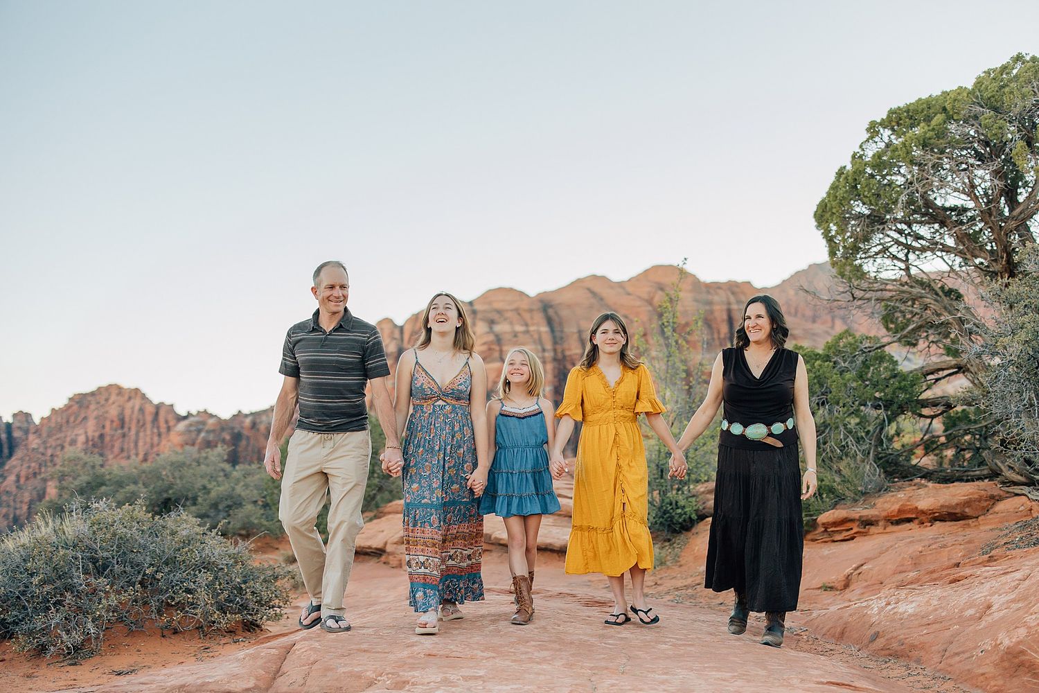 Group of people walking along scenic red rock trails in Snow Canyon State Park during sunset.