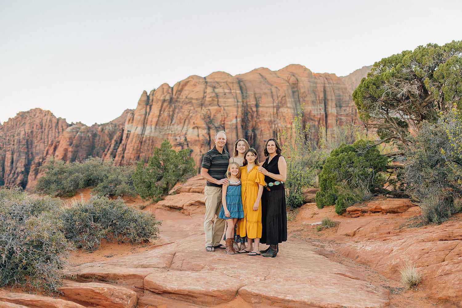 People pose together against stunning red rock formations in a desert landscape at sunset.