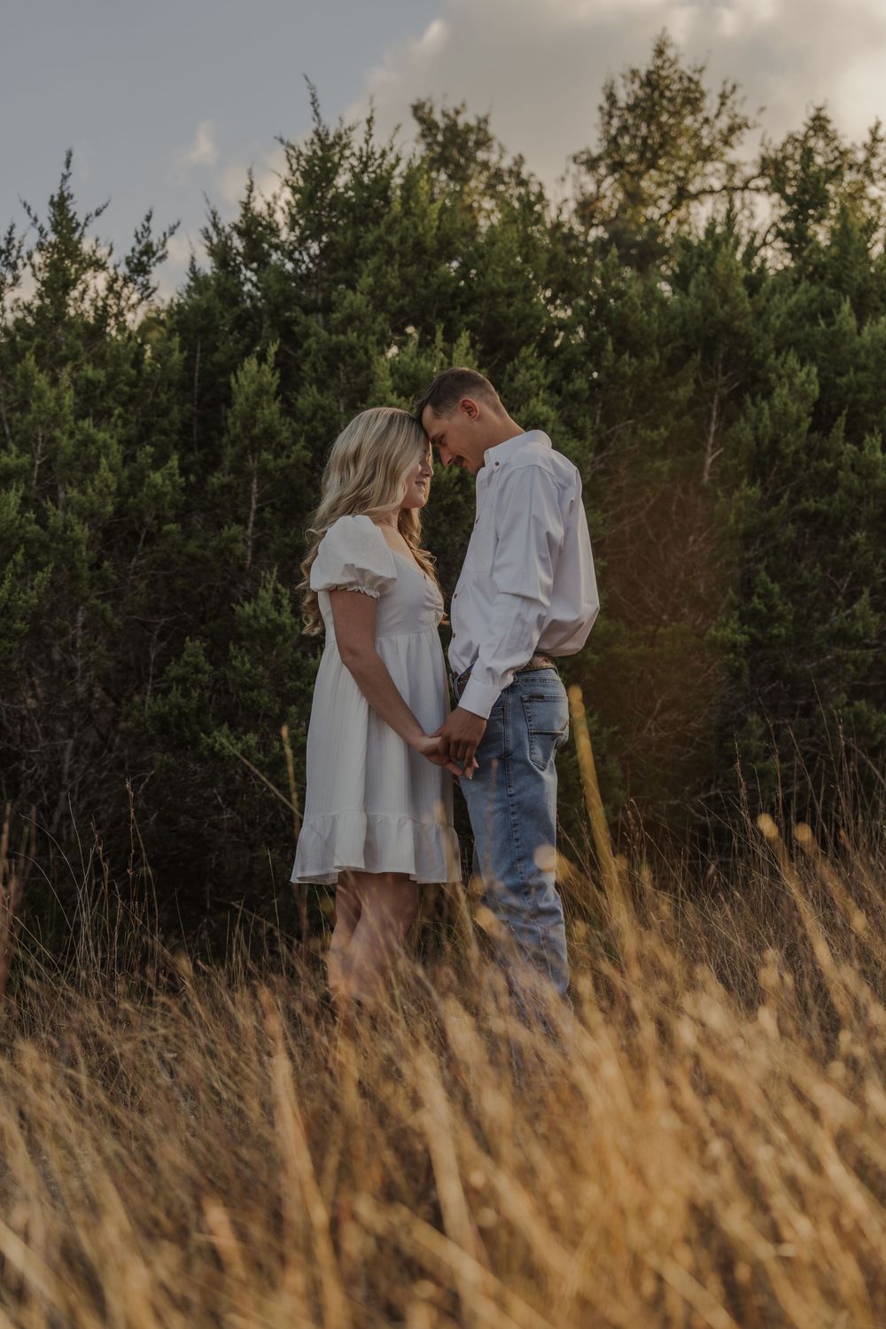 A couple shares an intimate moment together in a field of tall golden grass at sunset.