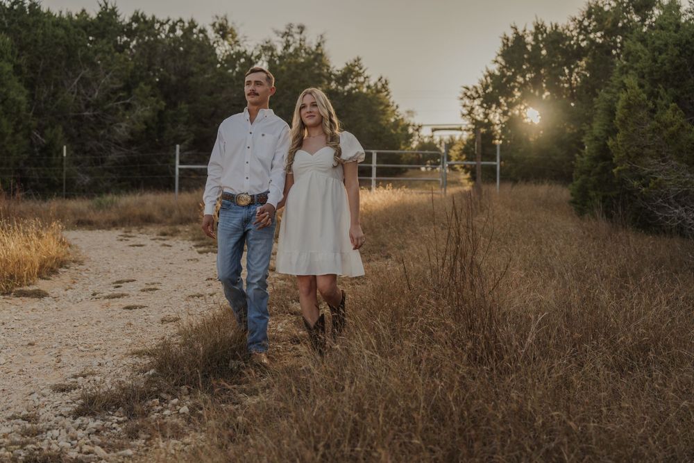 Romantic sunset engagement photoshoot with couple walking through tall grass in a natural outdoor setting.
