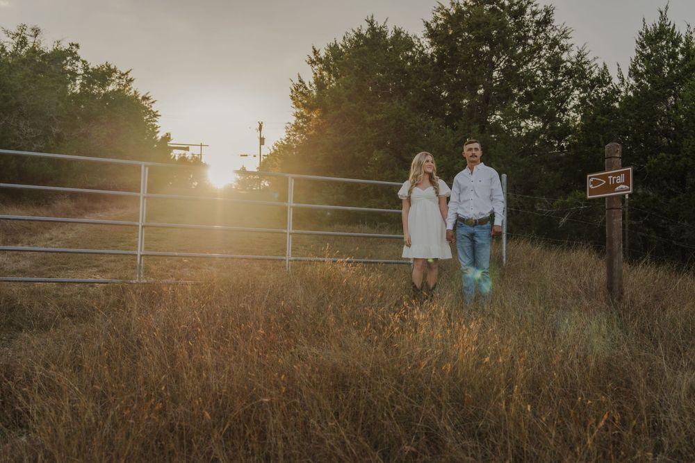 Couple shares tender moment at sunset by metal fence in rural field setting.