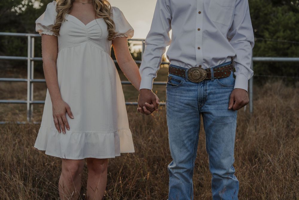 A couple holding hands in a country setting, with a white dress and casual western wear visible against a rustic backdrop.