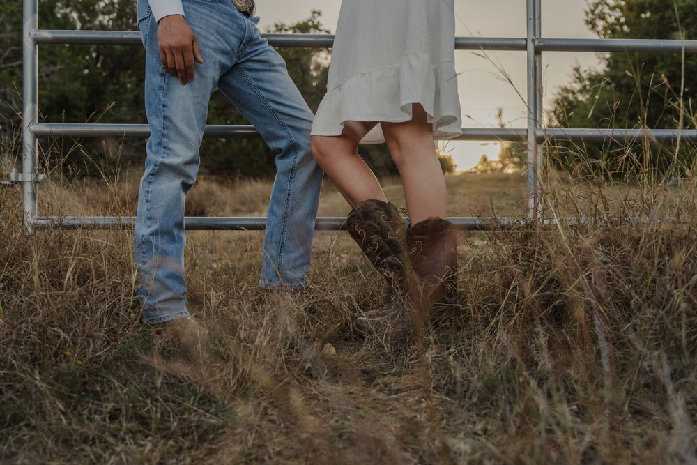 A pair of legs in blue jeans and brown boots stand on wooden planks outdoors.