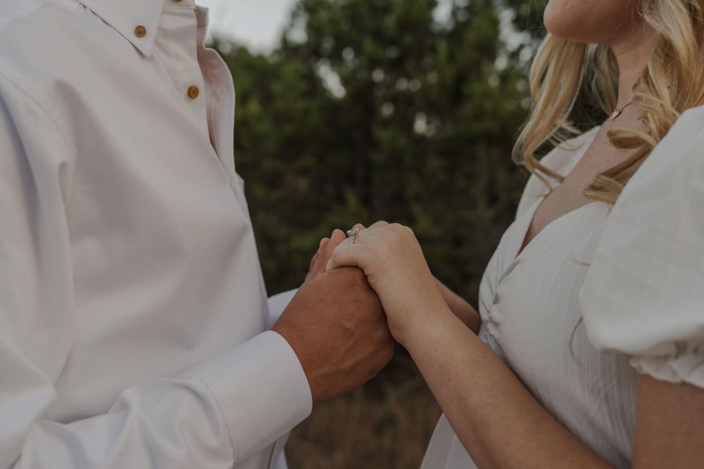 A romantic outdoor wedding scene with a couple embracing in white attire surrounded by natural greenery.