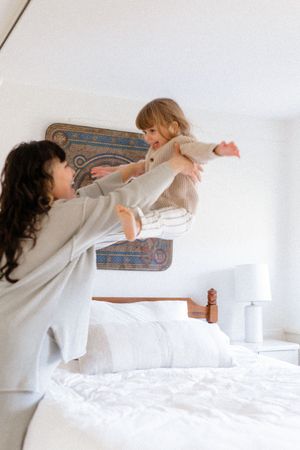 Playful sequence of two people in white having a pillow fight on a bed with decorative wall art.
