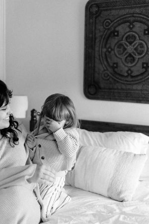 Candid moments captured of people laughing and playing on white bedding with dark wall decorations.
