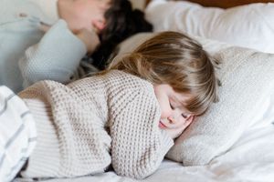 Child sleeping peacefully in bed wearing a cozy knit sweater among white pillows.