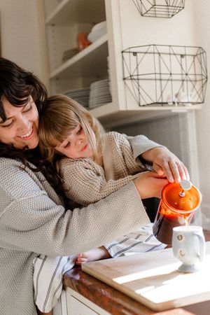 Shared moment of joy while pouring orange juice together in a bright kitchen.