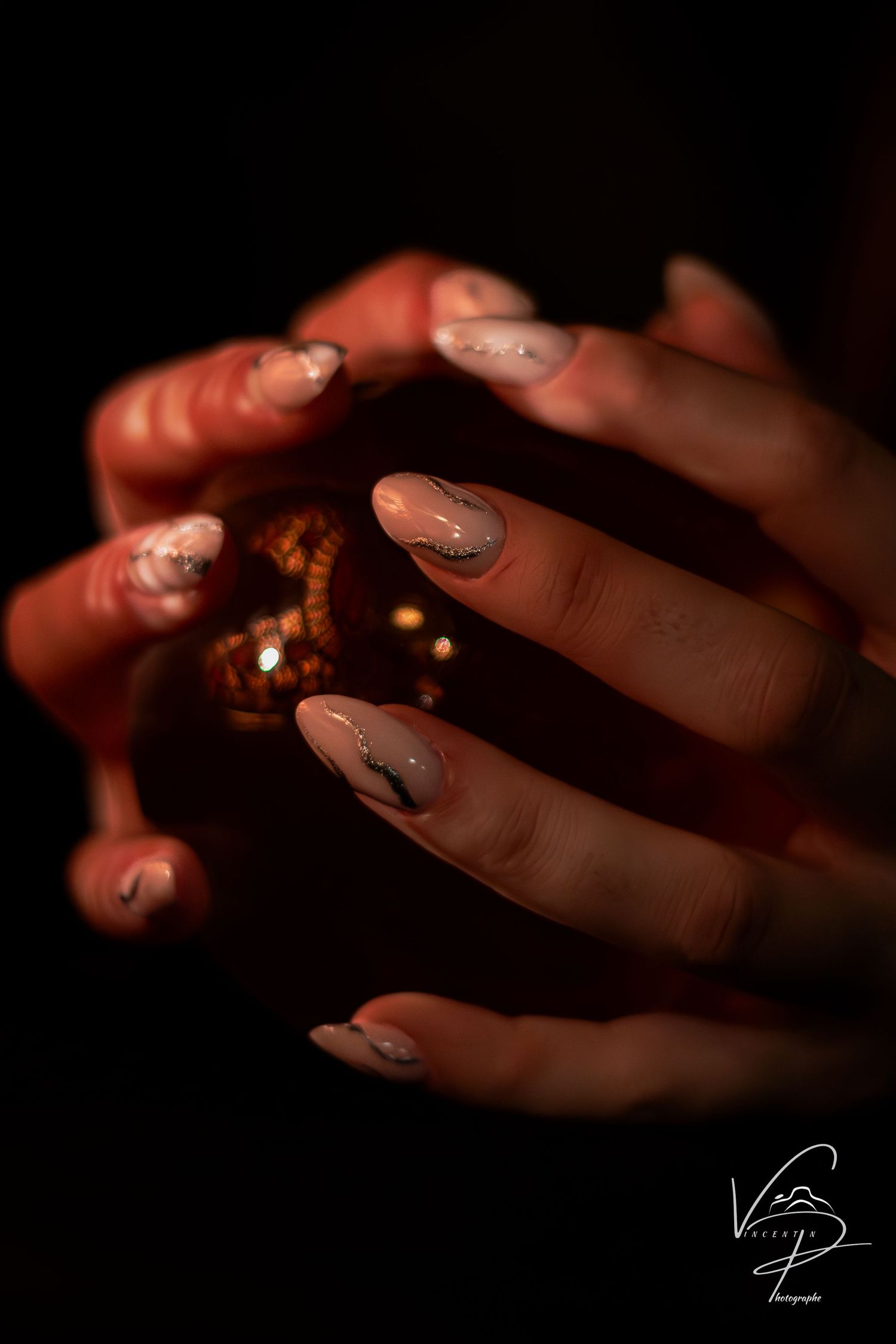 Close-up of manicured nails with sparkly polish reflecting warm light.
