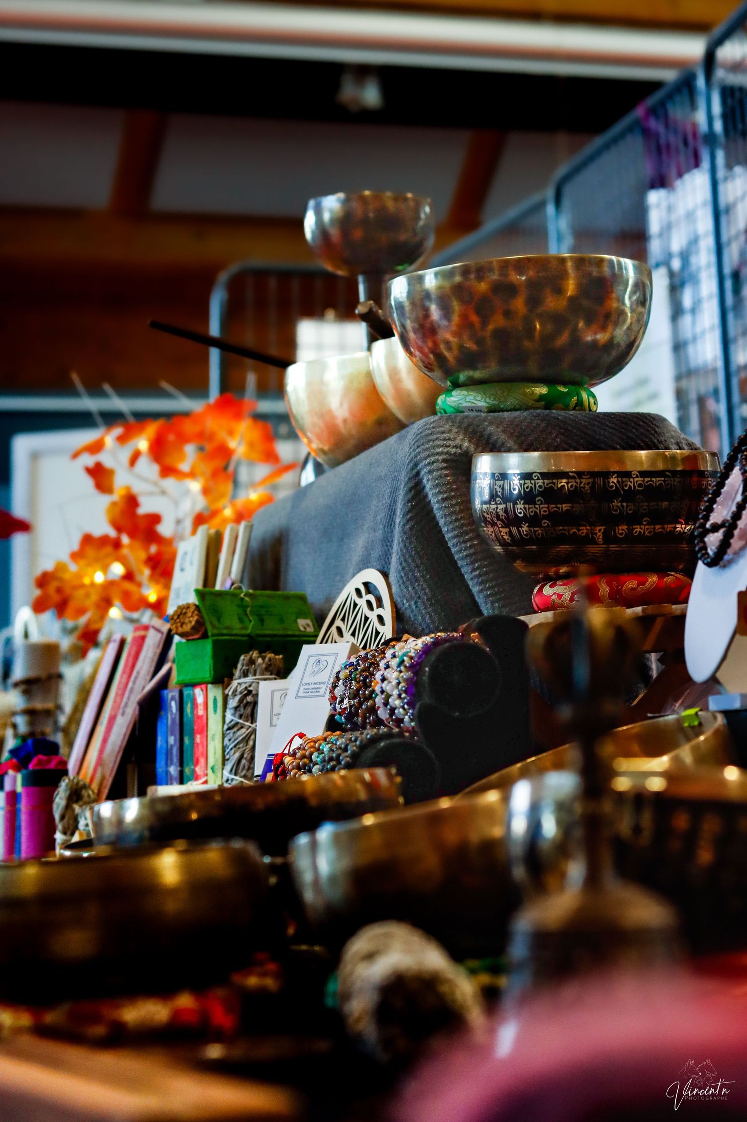 Decorative singing bowls and spiritual items arranged on a shelf with autumn-colored flowers in background.