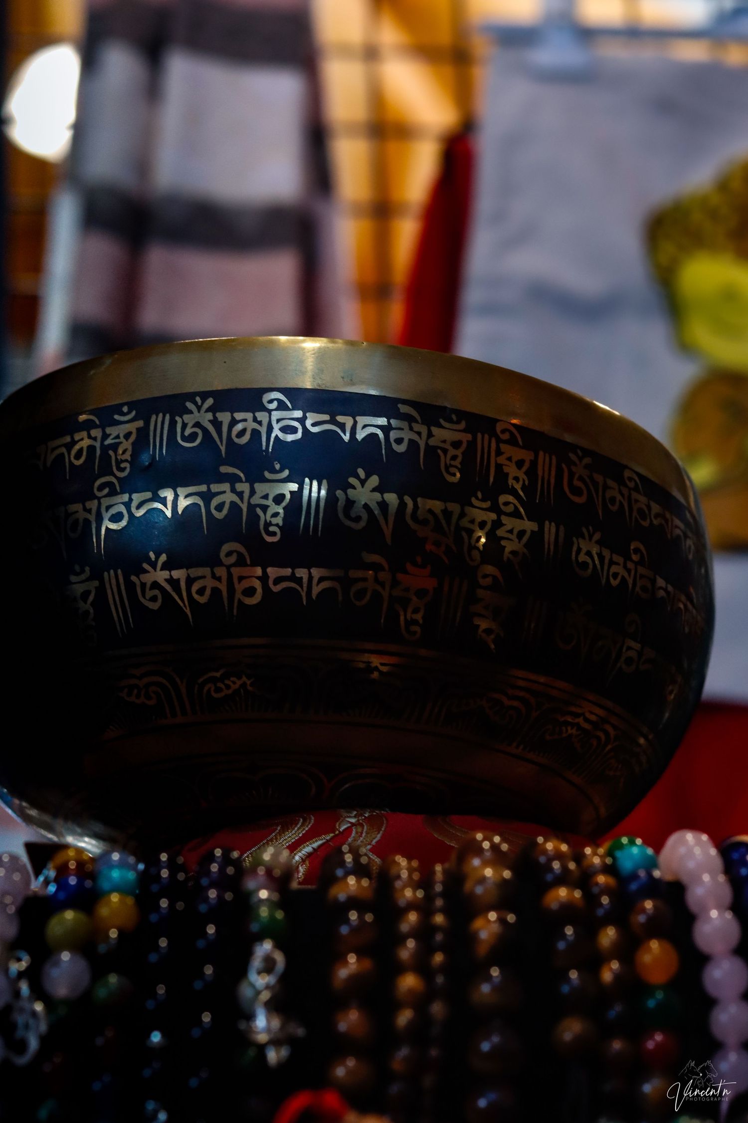 Traditional Tibetan singing bowl with carved Sanskrit inscriptions displayed with colorful prayer beads.