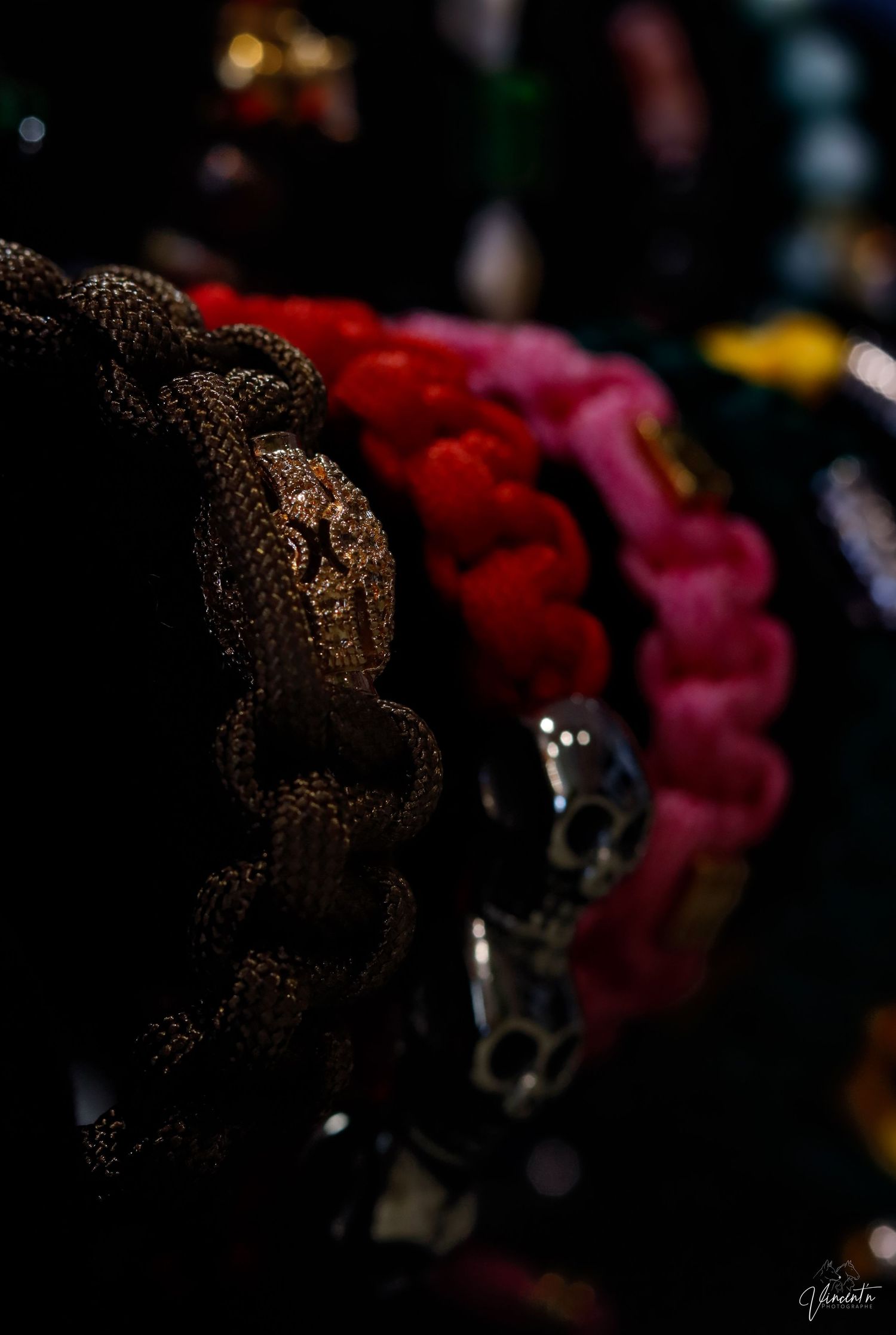Close-up of braided paracord bracelets in brown, red, and pink colors against dark background.