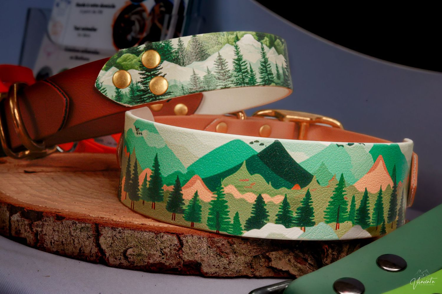 Hand-painted leather dog collars featuring mountain and forest landscapes on wood slice display.