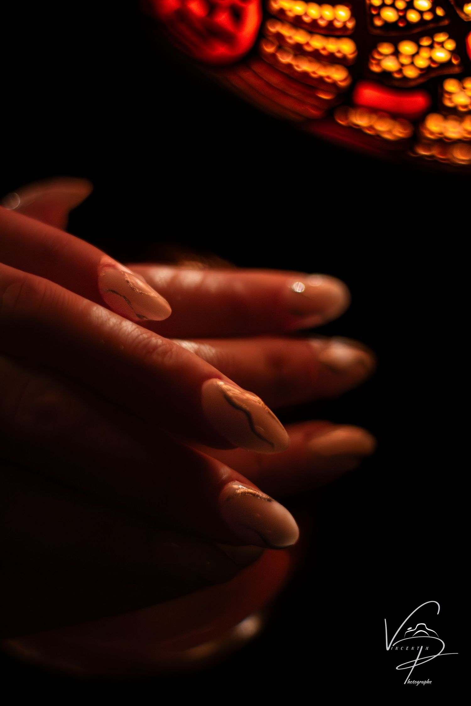Hands reaching towards a warm glowing carved lamp in dark ambiance.