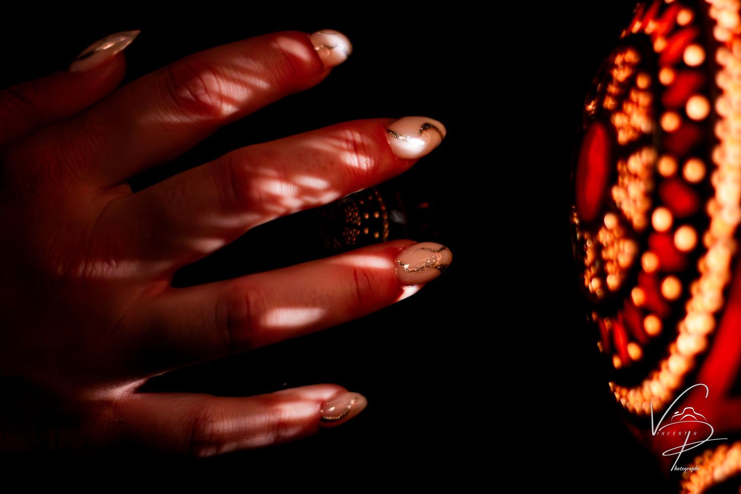 Hands reaching towards glowing red ornamental lights in darkness.