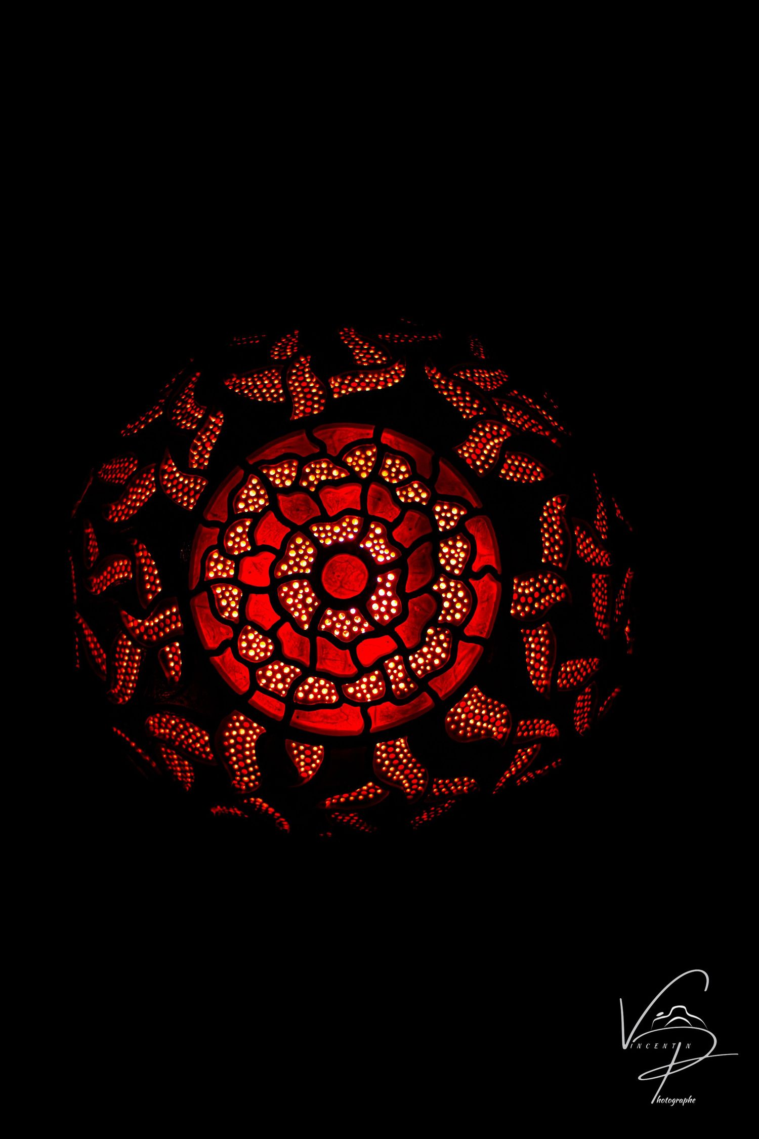 Red illuminated gourd lamp with intricate spiral pattern casting warm glow in darkness.