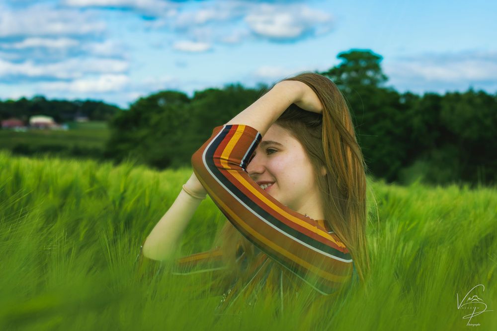 Artistic portrait in tall green grass field under blue summer sky.