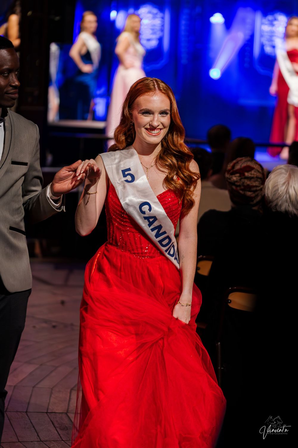 Elegant red ball gown twirls on stage with blue lighting effects.