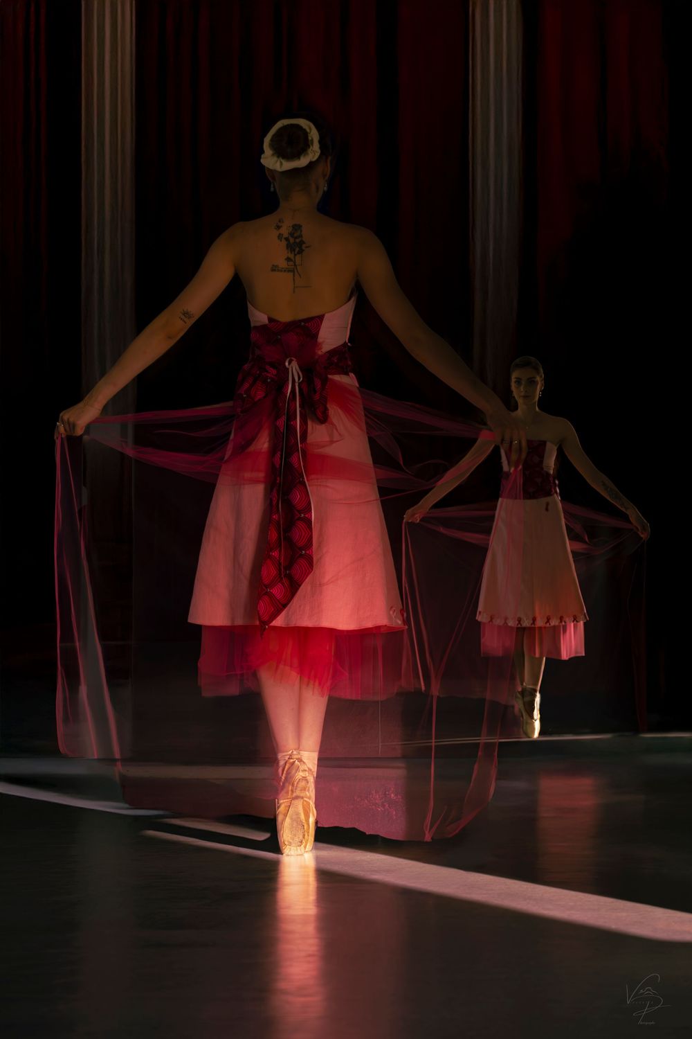 Dramatic stage performance featuring a dancer in a pink dress illuminated by red spotlights.