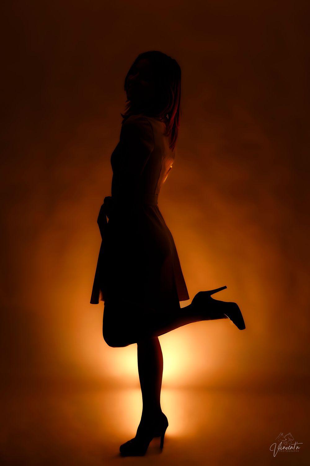 Silhouette of figure in heels against warm orange backlight creating dramatic shadow.